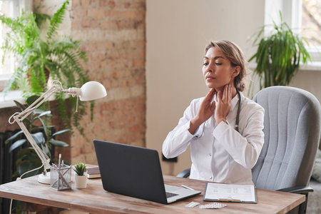 Modern female doctor sitting at desk in office demonstrating how to palpate neck lymph nodes on...