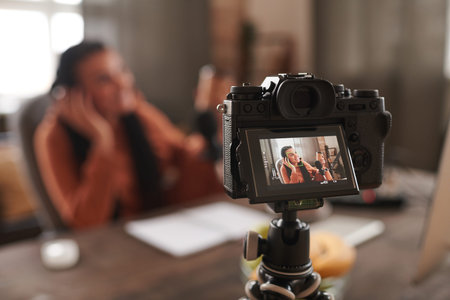 Horizontal shot of young woman with afro braids sitting at desk shooting video for blog on camera,...