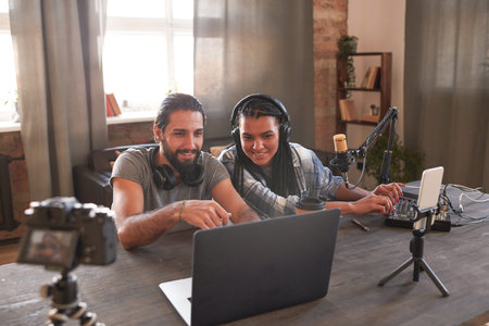 Horizontal high angle shot of stylish young man and woman sitting at desk in loft room creating funny content for their video blogの写真素材