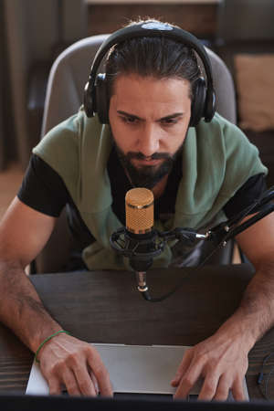 Vertical high angle portrait of serious Middle Eastern male influencer sitting at desk checking something on laptopの写真素材