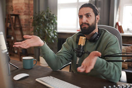 Horizontal medium portrait of young Middle Eastern man with beard on face sitting at desk reacting to comments to his video contentの写真素材