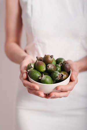 Vertical medium section shot of unrecognizable young woman wearing white dress holding bowl full of pineapple guava fruits, copy spaceの写真素材
