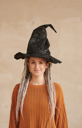 Portrait of smiling young woman with white dreads wearing witches hat standing against isolated...