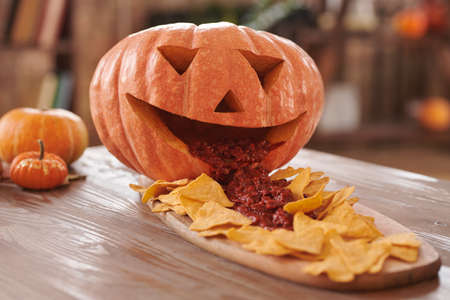 Close-up of Halloween nachos and sauce pouring from carved pumpkin on wooden boardの写真素材