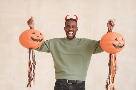 Portrait of emotional excited young Black man with beard holding Halloween paper lanterns against isolated backgroundの写真素材