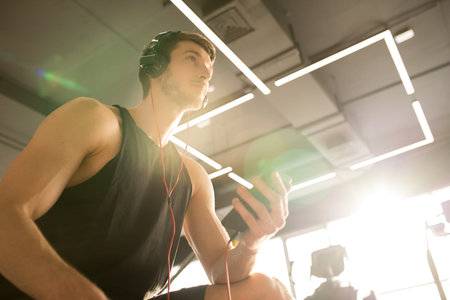 Young sportsman sitting in headphones and listening to music using his mobile phone