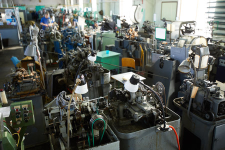 General view of clock factory shop full of machines with electric lamps used for production of clock...
