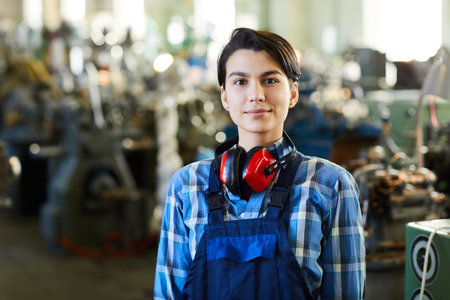 Content attractive masculine woman with short hair wearing ear protectors on neck standing at...