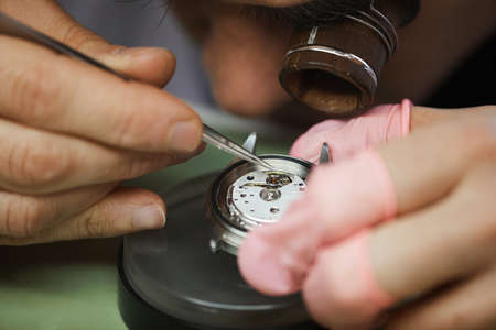 Close-up of concentrated engineer in monocular loupe on eye using tweezer while adjusting cog of wristwatchの写真素材