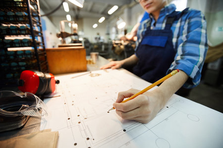 Close-up of busy engineer standing at desk and making points on technical card while working at...