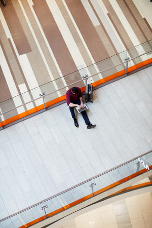 Directly above view of busy young man sitting on floor in airport lobby and typing on laptop while working remotelyの写真素材