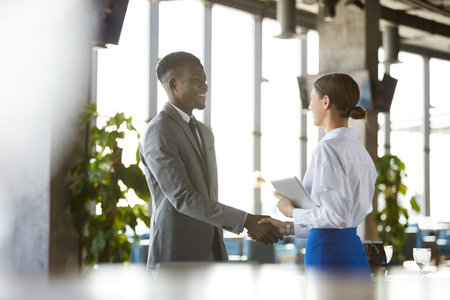 Collaboration with businessman of African race: young female manager in white blouse holding tablet...
