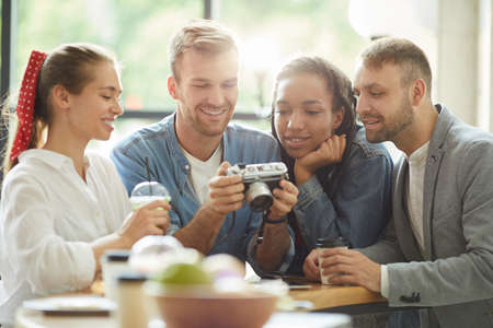 Content young multi-ethnic friends in casual clothing standing at counter in fast food cafe and choosing joint photo on camera screenの写真素材
