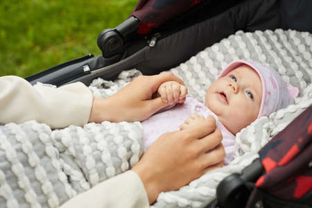 Small baby outside in black stroller in white hat and under grey blanket having a walk with motherの写真素材