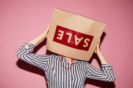 Unrecognizable woman in stripped shirt being excited about sale wearing paper bag on headの写真素材