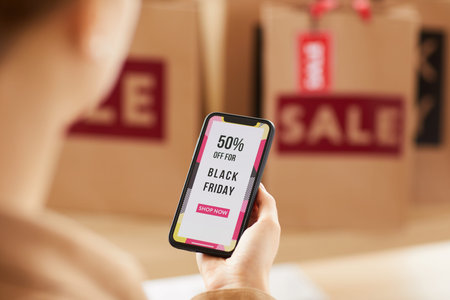 Over shoulder view of unrecognizable woman viewing bright online shopping poster on smartphone