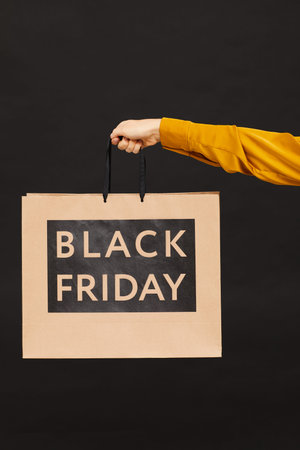 Close-up of unrecognizable woman in blouse holding shopping bag against black background, good offer...