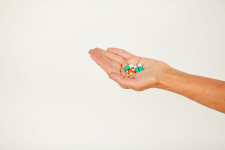 Close-up of unrecognizable person holding handful of various pills and antibiotics against white...