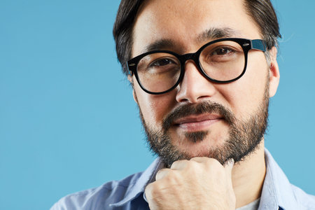 Asian bearded man in glasses standing against blue background