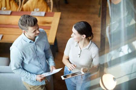 Above view of cheerful young marketing specialists standing in modern cafe and sharing product...