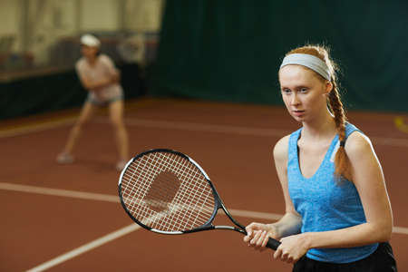 Serious concentrated professional tennis player in workout headband standing at court and gripping racket while playing doubles tennisの写真素材