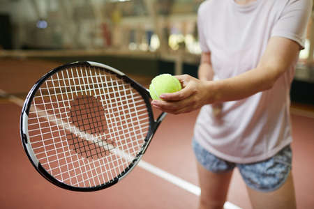 Close-up of unrecognizable woman in loose tshirt standing on indoors court and holding green ball while preparing for serving tennis ballの写真素材