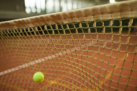 Close-up of tennis ball hitting net for fault, focus on tennis net on indoor court, copy spaceの写真素材
