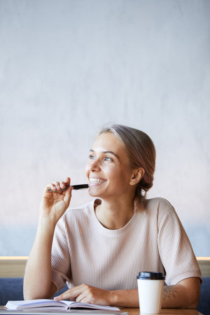 Dreamy excited freelance journalist with ash-colored hair sitting at table and thinking of new ideas...