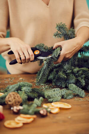 Close-up of unrecognizable woman standing at wooden table and using secateurs while cutting fir twig for Christmas wreathの写真素材