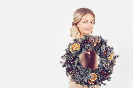 Portrait of content beautiful young blonde woman standing against white background and showing Christmas door decorationの写真素材