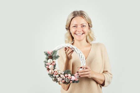 Portrait of cheerful excited beautiful young woman with blond hair standing against isolated background and holding artificial Christmas wreathの写真素材
