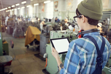Rear view of hipster factory supervisor using digital tablet while controlling production processes at factoryの写真素材