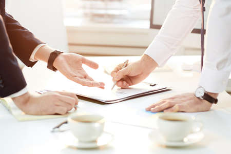 Close-up of unrecognizable business colleagues standing at table and discussing analytical points while viewing papers togetherの写真素材