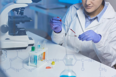 Close-up of concentrated lab technician sitting at desk and dropping blood on microscope slide while...