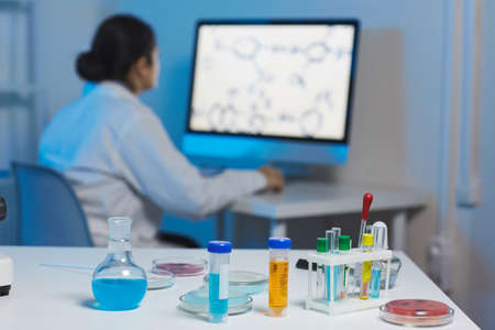 Chemical laboratory background of medical and biological samples in test tubes placed on white table, woman working with computer in backgroundの写真素材
