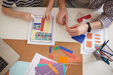 Above view of father and son sitting at table with colorful paper parts and gluing paper on tablet pattern for school projectの写真素材