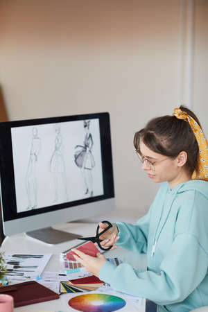 Content young woman with hair scarf ponytail sitting at desk with computer and preparing fabric patterns in workshopの写真素材
