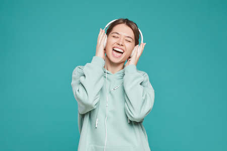 Happy carefree hipster girl in hoodie wearing headphones and singing out loud while listening to music, copy spaceの写真素材