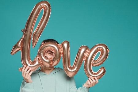 Portrait of playful young woman in hoodie standing against teal background and looking through...