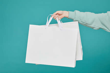 Close-up of unrecognizable woman in teal sweater holding white shopping bags against isolated backgroundの写真素材