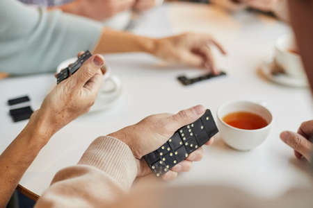 Close-up of elderly woman sitting at table and holding domino pieces in hand, she participating in domino tournament in retirement homeの写真素材