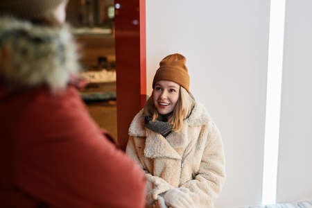 Horizontal over-the-shoulder shot of young Caucasian woman sitting outdoors on winter evening chatting with her boyfriend standing in front of herの写真素材
