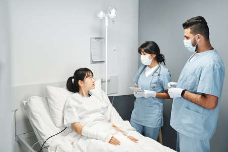 Two doctors working in emergency room with young Asian patient asking questions about health stateの写真素材