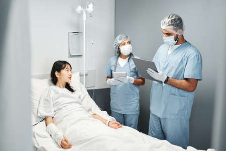 Two modern medical specialists working in emergency room with young Asian woman after accidentの写真素材