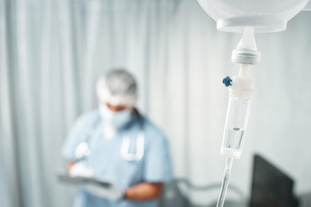 Horizontal selective focus shot of transparent bag full of medication fluid on pole connected with...