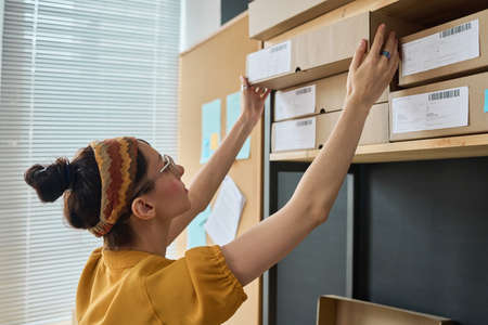 Young woman taking parcel in cardboard box from the shelf for deliveringの写真素材