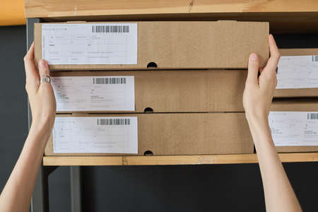 Close-up of courier taking parcel in cardboard box from high shelf to deliver to the addresseeの写真素材