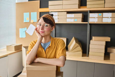 Portrait of female warehouse worker looking at camera while packing parcels in storageの写真素材