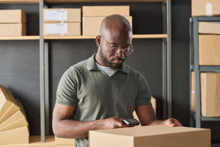 African warehouse worker scanning parcel with scanner to check track number before deliveringの写真素材