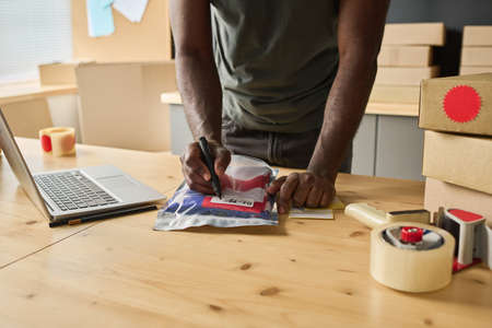Close-up of African man making notes on packet with order at table while distributing parcels to addressesの写真素材